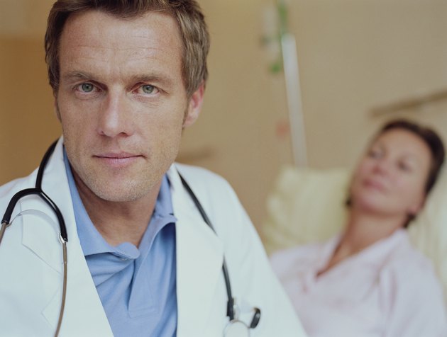 Mature male doctor by female patient lying in hospital bed