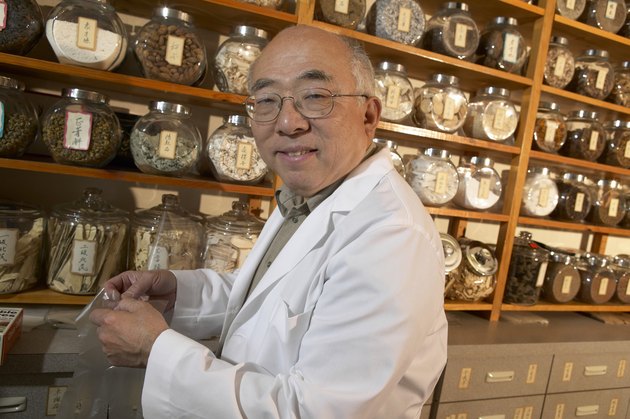 Senior Chinese-herbalist in store, holding plastic glove, smiling, portrait