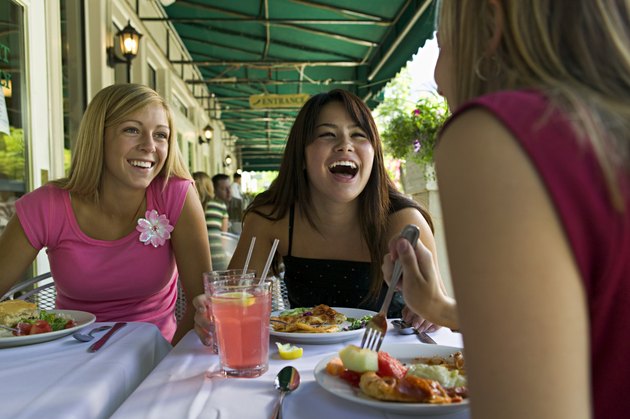 lifestyle portrait of a group of three teenage female friends as they eat at a sidewalk cafe