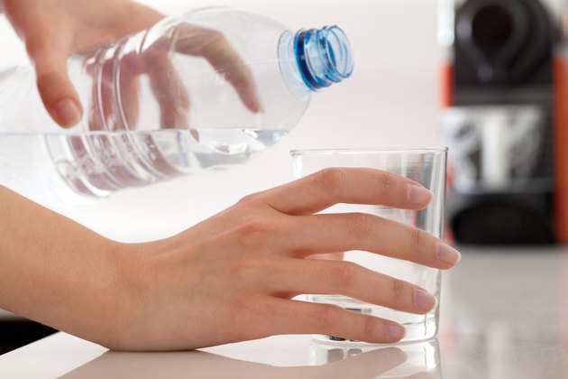 Female hands pouring bottled water into glass
