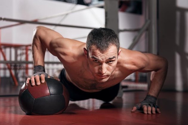 Do your best. Muscular man doing push-up with the help of special fitness ball and looking forward.
