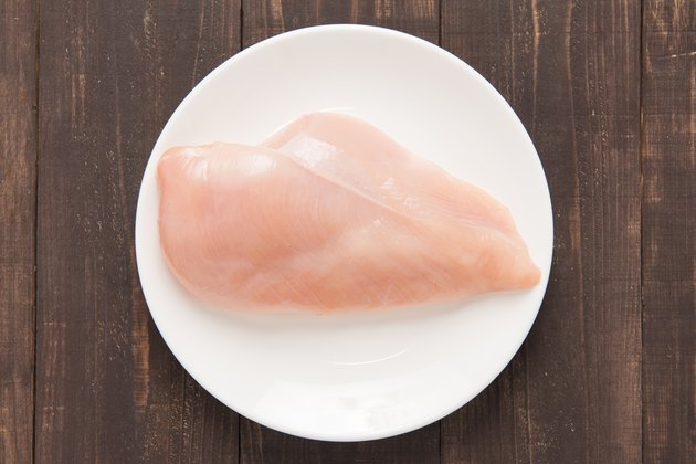 Raw chicken breast fillets on white dish.