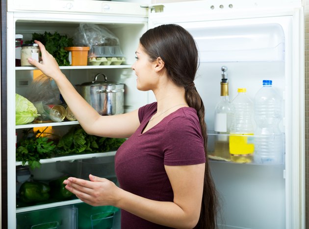 Positive housewife standing near filled fridge