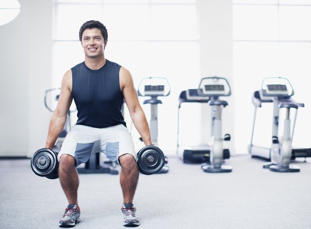 Smiling man doing squats with dumbbells in gymnasium