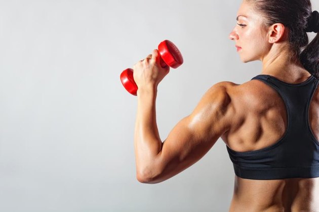 Fitness woman with barbells on grey background