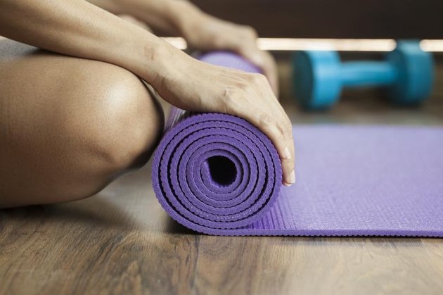 A woman unrolls an exercise or yoga mat.