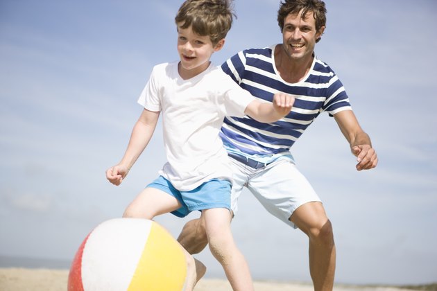 Father and son playing with ball on beach
