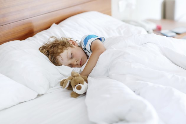 Adorable kid boy after sleeping in white bed with toy