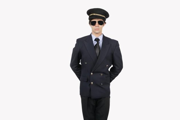 Young man in pilot uniform standing against gray background