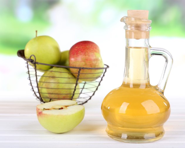 Apple cider vinegar in bottle and apples, on table