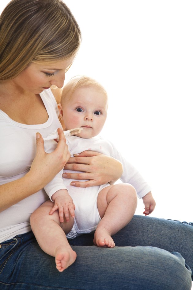 Mother giving vitamins to infant girl on white