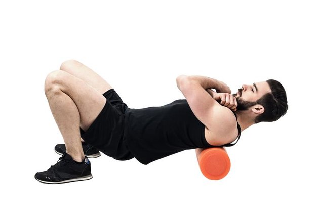 Athlete massaging upper back muscles with foam roller. Full body length portrait isolated on white studio background.