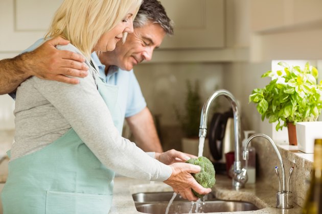 Happy mature couple washing broccoli