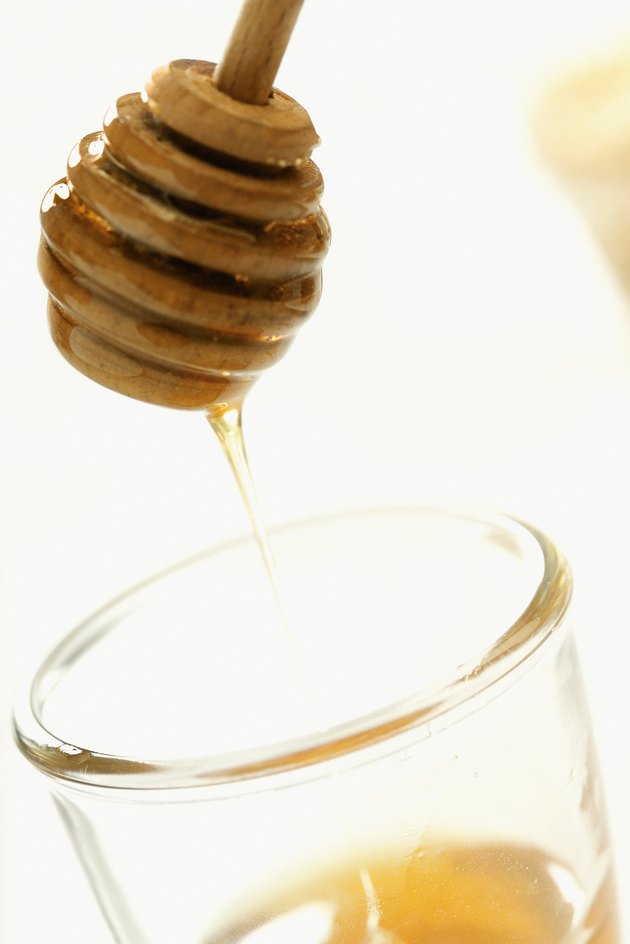Honey dipper above jar of honey, close-up tilt