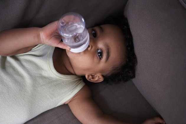 baby drinking water lying on a sofa
