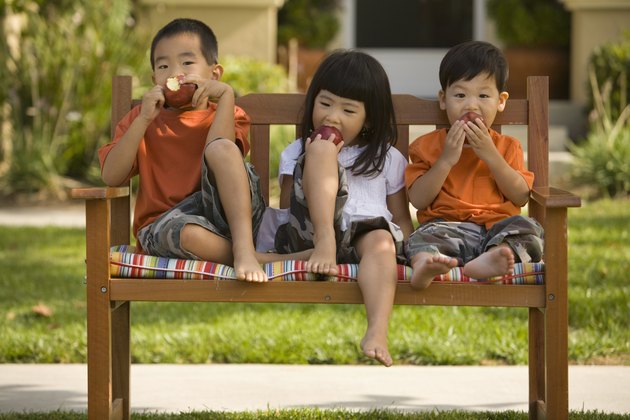 Asian siblings eating apples on bench