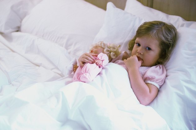 High angle view of a baby girl with a doll lying in bed
