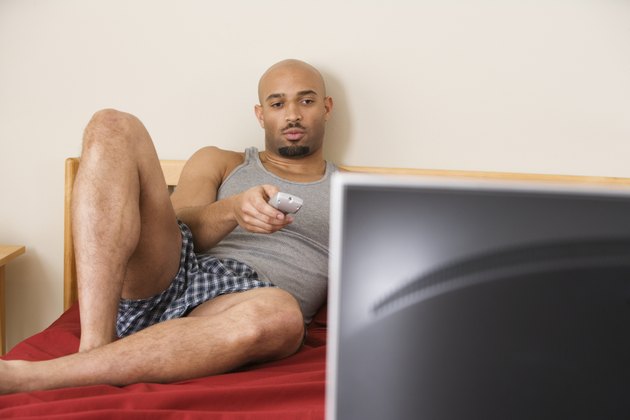 African man watching television in bed