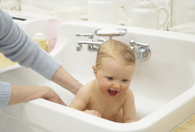 Grandmother's hands bathing granddaughter (9-12 months) in sink,