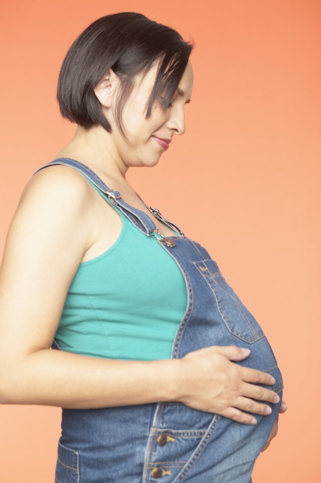 Side profile of a pregnant young woman holding her belly