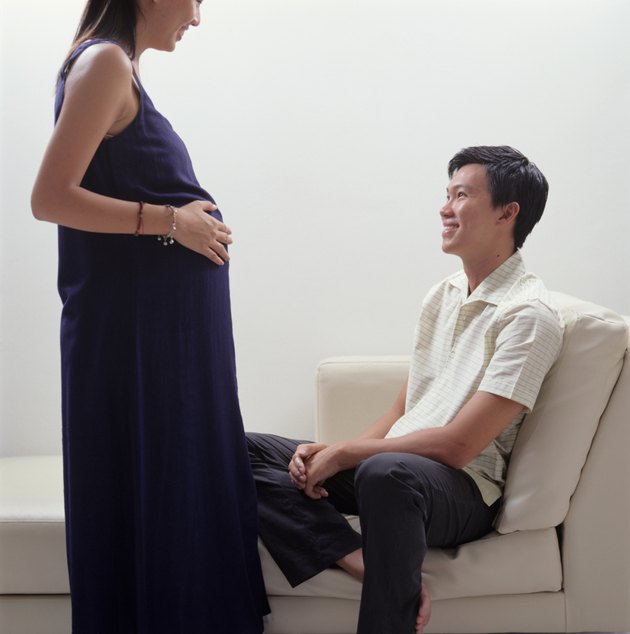 Pregnant woman standing talking to husband sitting on couch