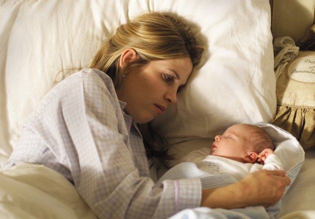 a young caucasian mother lies in the bed alongside her newborn baby