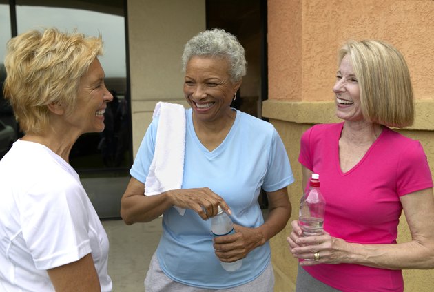 Three mature women holding water bottles outdoors, laughing