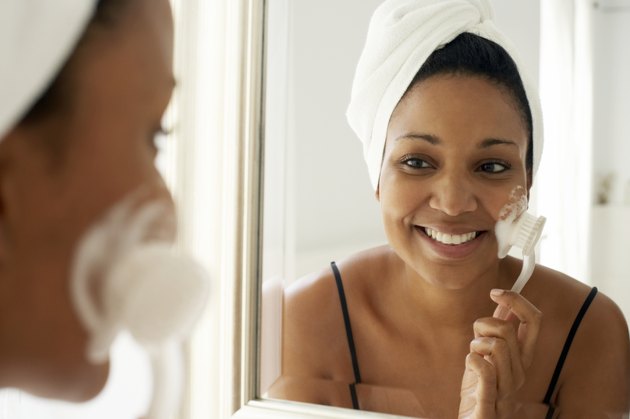 Young woman brushing face with toothbrush, reflection in mirror