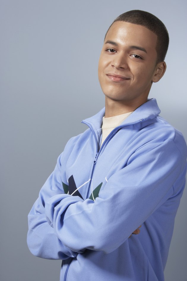 Teenage boy (16-18) against blue background, arms folded, portrait