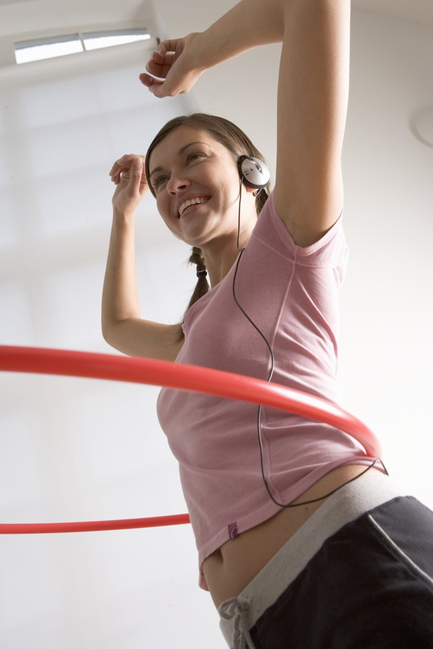 Woman spinning plastic hoop around waist, wearing headphones, smiling
