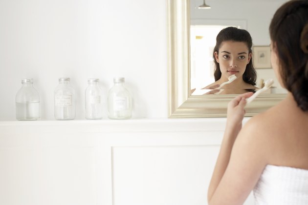 Young woman holding toothbrush, looking in mirror, rear view
