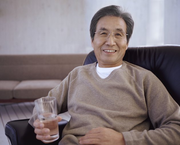 Portrait of a Senior Man Sitting on a Chair Holding a Glass of Water