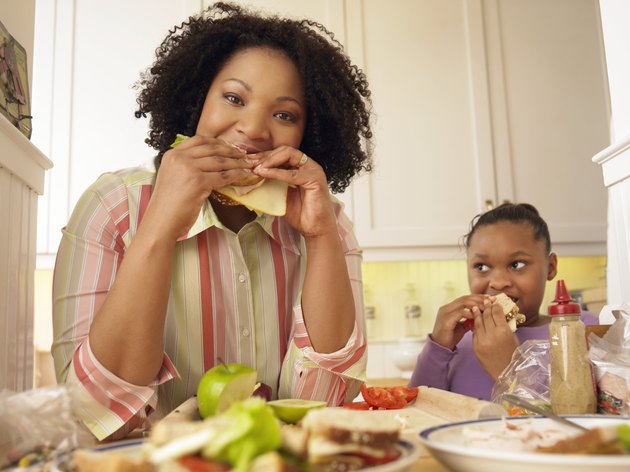 Mother and Her Young Daughter Stand in the Kitchen Eating Cheese Sandwiches for Lunch