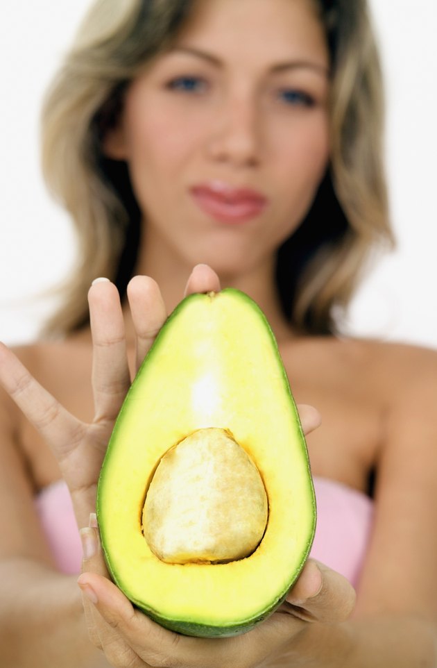 Young woman holding out half of an avocado, close-up, selective focus, focus on hand and avocado