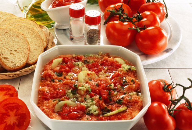 close-up of a tomato based dish served beside whole tomatoes and bread
