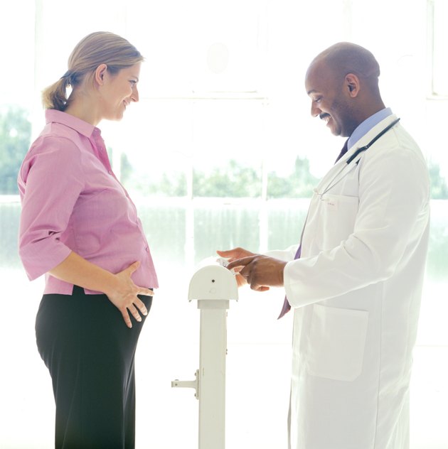 portrait of a young pregnant woman getting her weight checked by a doctor