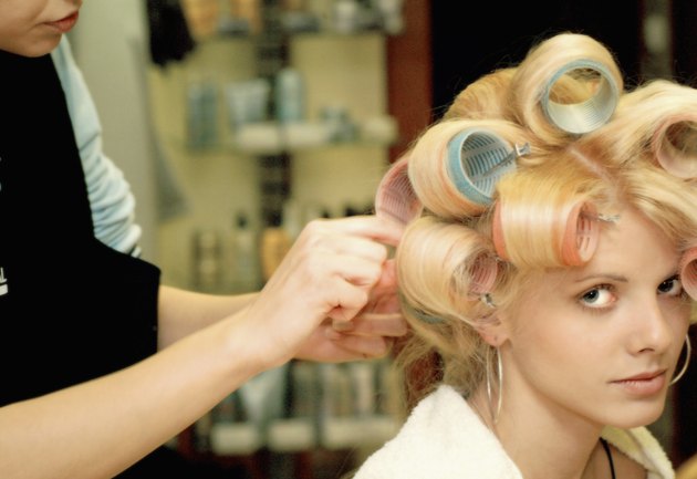 Female hairdresser adjusting curlers in a mid adult woman's hair