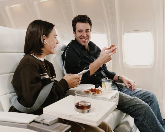 Man Sits in a Plane Seat Next to His Son, Sharing Headphones and Eating a Snack