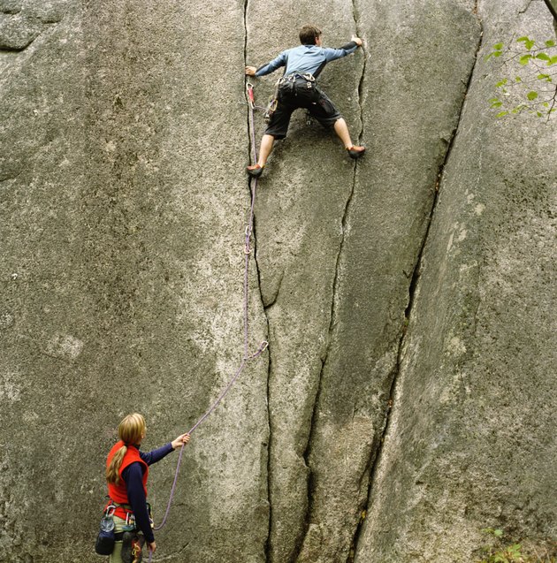 Woman holding rope, looking upward at partner climbing rock wall