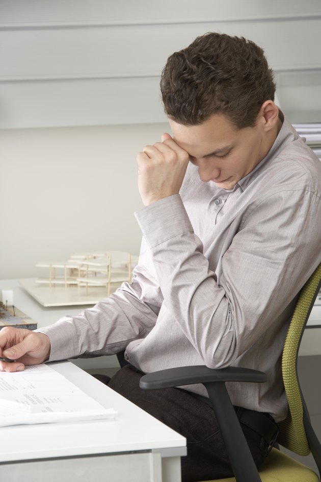 Young businessman at desk, hand by face