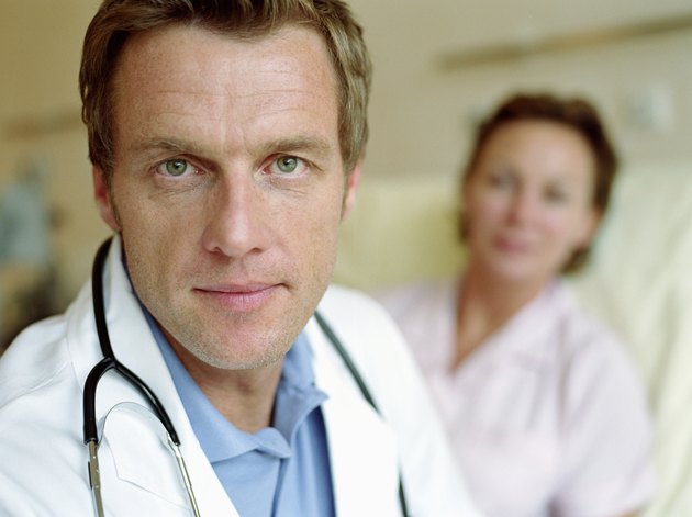 Mature male doctor by female patient lying in hospital bed, portrait