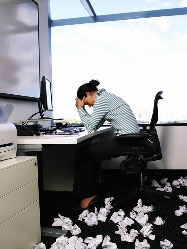 Woman sitting at desk by crumpled papers on floor