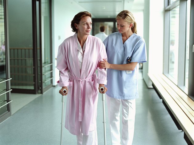 Female nurse holding patient using crutches in hospital corridor