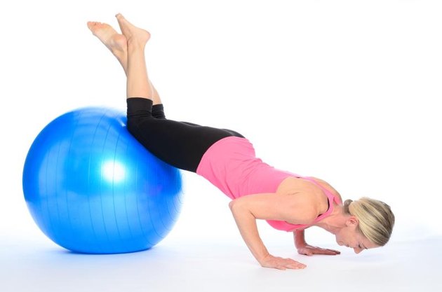 Athletic woman doing pilates exercises balancing with her knees on the ball doing press ups while controlling and strengthening her muscles, over white