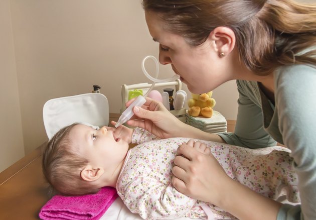 Mother cleaning mucus of baby with nasal aspirator