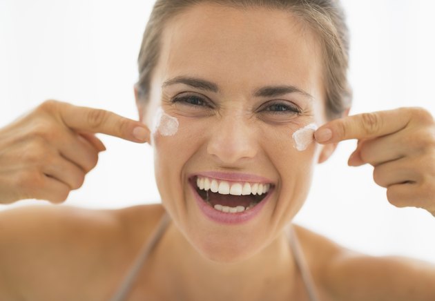 Happy woman having fun time while applying cream in bathroom