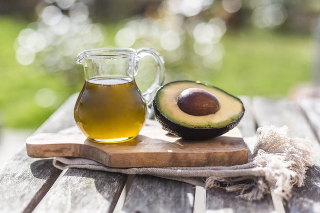 Half of avocado and glass jug of avocado oil on wooden board