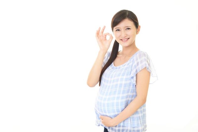 Smiling pregnant woman touching tummy against white background