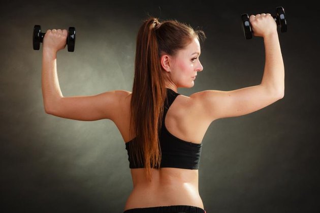 Bodybuilding. Strong fit woman exercising with dumbbells. Muscular long hair girl lifting weights on black