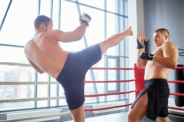 Portrait of shirtless wrestler fighting with opponent in boxing ring at fight practice: evading high kick in head